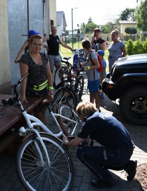 Policjantka znakuje rower podczas festynu w Wąwelnie. W tle kolejne osoby czekają na znakowanie swoich rowerow