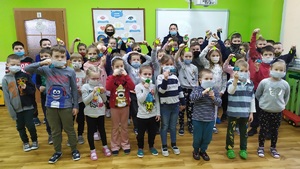 Wspólne zdjęcie z uczniami z Dąbrówki. Z przodu stoją dzieci, z tyłu dwie policjantki. Uczniowie trzymają w rękach otrzymane od funkcjonariuszek zawieszki odblaskowe.