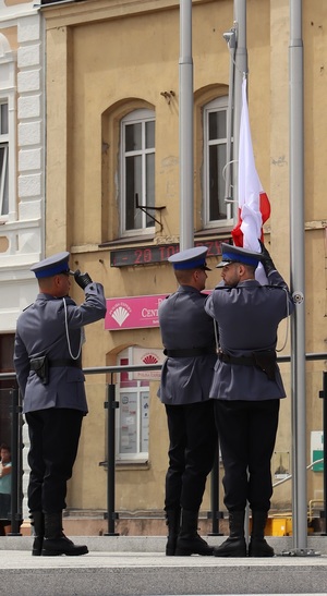 Trzech policjantów stoi przy maszcie i ponosi flagę państwowa na maszt.