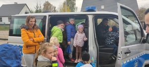 Plac przed Szkoła Podstawowa w Zalesiu. Dzieci odpadają z bliska policyjny radiowóz. Cześć dzieci znajduje się wewnątrz radiowozu, a druga cześć stoi przed pojazdem. Policjant siedzi na miejscu kierowcy.