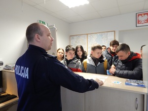 Stanowisko kierowania w komendzie. Policjant stoi twarzą do uczni i opowiada o zadaniach i obowiązkach dyżurnego.