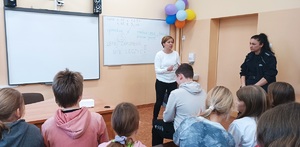 Pomieszczenie sali lekcyjnej. Prelekcje prowadzi przedstawicielka sanepidu. Stoi przodem do zdjęcia. Obok niej stoi policjantka. Uczniowie siedzą w ławkach szkolnych, twarzami zwróceni do gości.