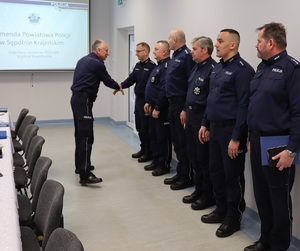 Świetlica w sępoleńskiej komendzie. Zastępca Komendanta Wojewódzkiego Policji w Bydgoszczy wita się z policjantami, którzy ustawieni są wzdłuż ściany. W tle widać prezentacje multimedialną.