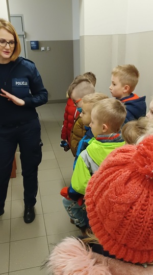 Pomieszczenia dla osób zatrzymanych w Komendzie Powiatowej Policji w Sępólnie Krajeńskim. Po lewej stronie zdjęcia stoi policjantka, po prawej dzieci ustawione w rzędzie.