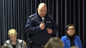 Miejsko-Gminny Ośrodek Kultury w Kamieniu Krajeńskim. Policjant stoi i przemawia przed mieszkańcami. Obok niego przy stole siedzą pozostali przedstawiciele instytucji.