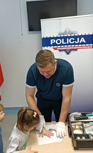 Policjant -technik kryminalistyki pokazuje dzieciom jak zabezpiecza się ślady dłoni.
