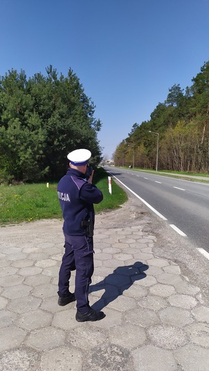 Policjant stoi przed jezdnią i mierzy prędkość za pomocą radaru