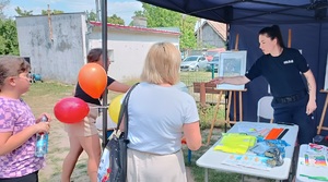 Policjantka wręcza odblaski uczestnikom festynu. W tle widać plakat z napisem zostań kimś wyjątkowym.