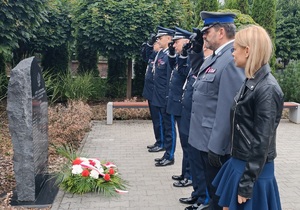Policjanci stoją przed pomnikiem pomordowanych policjantów powiatu sępoleńskiego razem z przedstawicielka związków zawodowych pracowników Policji.