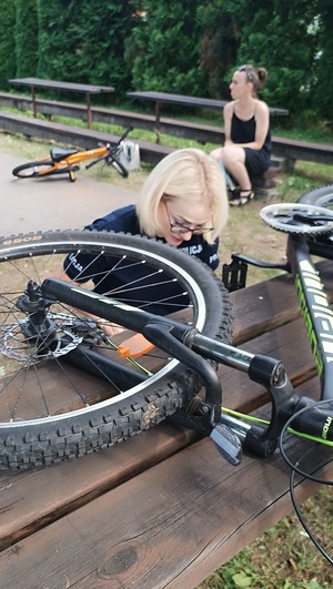 Teren ogródków działkowych Zacisze w Sępólnie Krajeńskim. Rower leży na stole. Za nim widać schylona policjantkę, a za nią w tle siedzącą na ławce kobietę.