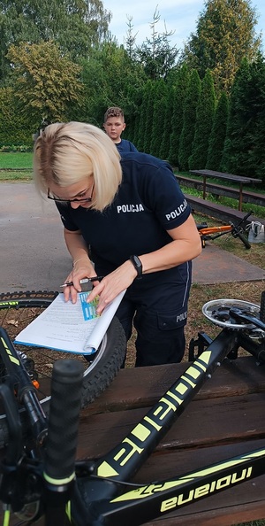 Teren ogródków działkowych Zacisze w Sępólnie Krajeńskim. Rower leży na stole. Za nim widać pochylającą się nad rowerem policjantkę. W tle widać zgromadzonych działkowców.