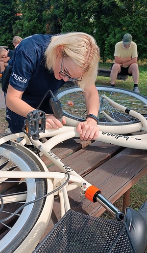 Teren ogródków działkowych Zacisze w Sępólnie Krajeńskim. Rower leży na stole. Za nim widać pochylającą się nad rowerem policjantkę z grawerem w ręku. W tle widać zgromadzonych działkowców.