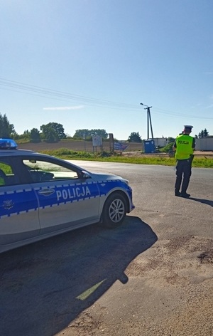 Policjant ruchu drogowego stoi przy drodze i dokonuje pomiaru prędkość pojazdów.