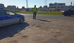 Policjant ruchu drogowego stoi przy drodze i zatrzymuje do kontroli nadjeżdżający pojazd.