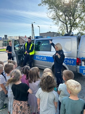 Policjanci pokazują radiowóz policyjny zgromadzonym wokół niego dzieciom.