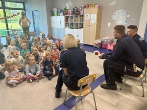 Policjanci siedzą na krzesełkach a przed nimi na podłodze siedzą dzieci.