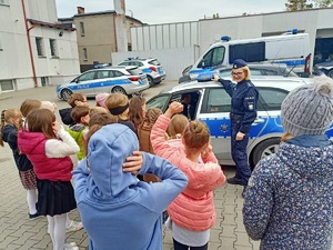 Policjantka pokazuje dzieciom radiowóz policyjny. Ma włączone sygnały dźwiękowe i świetlne.