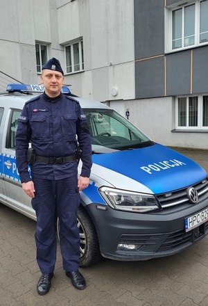 Na zdjęciu młodszy aspirant Zbigniew Pastwik. Za nim stoi zaparkowany radiowóz policyjny.
