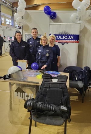 Wspólne zdjęcie policjantek wraz z Komendantem oraz policyjna kadrową przy stoisku wystawionym podczas targów pracy.