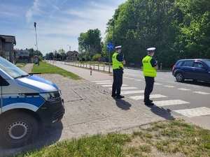 Policjanci stoją przy ulicy. Obserwują ruch drogowy.