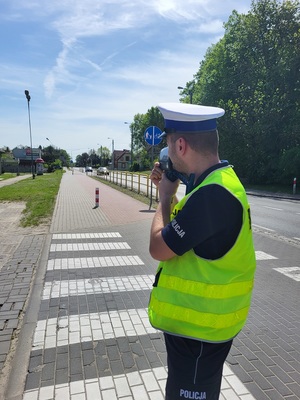 Policjant dokonuje pomiaru prędkości. W rękach trzyma miernik prędkości.