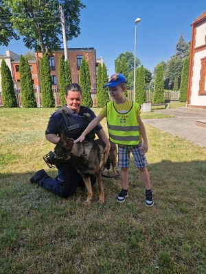 Przedszkolak w obecności policjantki dotyka psa policyjnego.