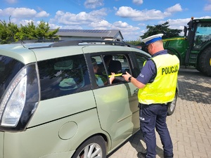 Policjant podczas działań Niechroniony Uczestnik Ruchu Drogowego. Wręcza pasażerowi auta odblask