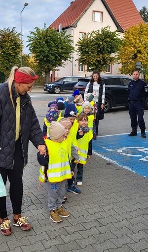 Przedszkolaki maszerują przez parking.