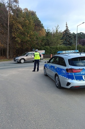 Policjant ruchu drogowego  stoi przy drodze  i kontroluje ruch drogowy.