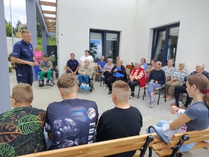 dzielnicowy na spotkaniu w Centrum Opiekuńczo mieszkalnym w Sępólnie Krajeński. Policjant stoi przed siedzącymi na krzesłach seniorami i dziećmi.