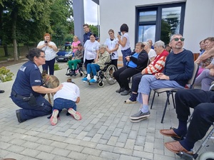 Spotkanie w Centrum Opiekuńczo mieszkalnym w Sępólnie Krajeński. Policjantka pokazuje razem z dzieckiem pozycje na żółwia. Pozostali uczestnicy siedzą przed nią na krzesłach.