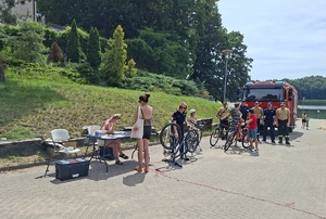 Policjantka znakuje rower. W oddali widać kolejkę do znakowania rowerów oraz pojazd straży pożarnej.
