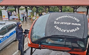 Policjantka stoi przy symulatorze dachowania. W tle widać policyjny radiowóz.