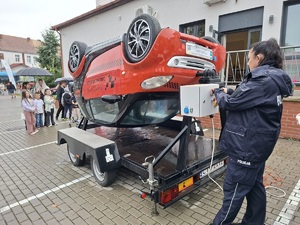 Policjantka stoi przy symulatorze dachowania. W tle widać kolejkę chętny osób do skorzystania z symulatora.