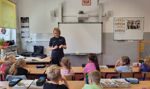 Policjantka stoi przed uczniami siedzącymi w ławkach szkolnych.
