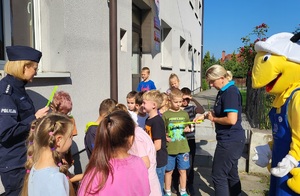 Policjantka wraz z przedstawicielem firmy mrówka rozdają odblaski uczniom