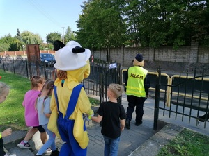 policjantka razem z maskotką mrówką wychodzą przez bramę w kierunku przejścia dla pieszych