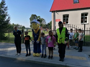Policjantka stoi przed przejściem razem z dziećmi i maskotka mrówką