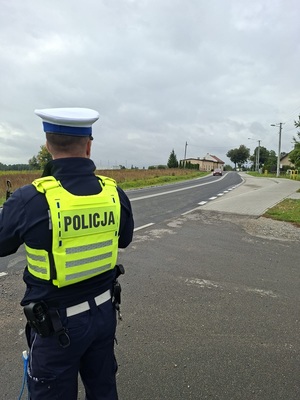 Policjant ruchu drogowego stoi przed jezdnię, która jadzie samochód.