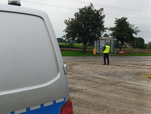 Policjant ruchu drogowego stoi przed jezdnia. W ręku trzyma miernik prędkości.