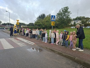 Policjantka rozmawia z dziećmi o zasadach bezpiecznej drogi do szkoły. Obok niej stoi maskotka Mrówki