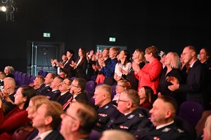 Sala kinowa w Centrum Kultury i Sztuki w Sępólnie Krajeńskim. Koncert z okazji 100-lecia Kobiet w Policji. Część uczestników koncertu stoi, pozostali siedzą. Zwróceni są bokiem do zdjęcia.