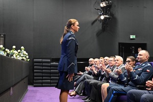 Zastępca Komendanta wojewódzkiego Policji w Gdańsku podczas przywitania przez lektora stoi przodem do widowni. Obok siedzą uczestnicy koncertu