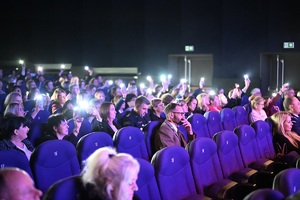 Ujęcie na siedzących na widowni uczestników koncertu. w rękach trzymają włączone latarki.