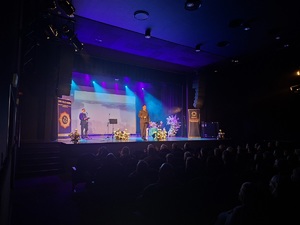 Sala kinowa w Centrum Kultury i Sztuki w Sępólnie Krajeńskim. Na scenie stoi dwóch policjantów, a z tyłu na sofie siedzą dwie policjantki oraz pracownik cywilny. W tle wyświetlany jest film promujący poszczególne gminy powiatu sępoleńskiego. Po bokach sceny  ustawione są banery promujące Komendę Powiatowa Policji w Sępólnie Krajeńskim oraz Niezależny Samorządny Związek Zawodowy Policjantów w Sępólnie Krajeńskim