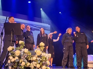 Sala kinowa w Centrum Kultury i Sztuki w Sępólnie Krajeńskim. Na scenie stoją wszyscy  śpiewający policjanci. W tle wyświetlany jest film promujący poszczególne gminy powiatu sępoleńskiego. Po bokach sceny  ustawione są banery promujące Komendę Powiatowa Policji w Sępólnie Krajeńskim oraz Niezależny Samorządny Związek Zawodowy Policjantów w Sępólnie Krajeńskim