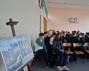 zdjęcie uczestników debaty siedzących na krzesłach. Zwróceni są twarzą do zdjęcia . z lewej stronie zdjęcia na stojaku stoi plakat promujący zawód policjanta.