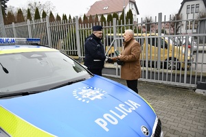 Uroczyste przekazanie radiowozu policyjnego w obecności samorządowców oraz kadry kierowniczej sępoleńskiej Policji. Na zdjęciu nowy radiowóz policyjny skoda octavia. Starosta wręcza opakowanie prezentowe z kluczykami do pojazdu w środku jednemu z policjantów.