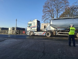 Policjant trzyma w ręku miernik prędkości. W tle pojazd ciężarowy.