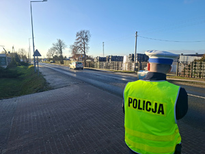 Policjant stoi przy drodze i kontroluje prędkość pojazdów.